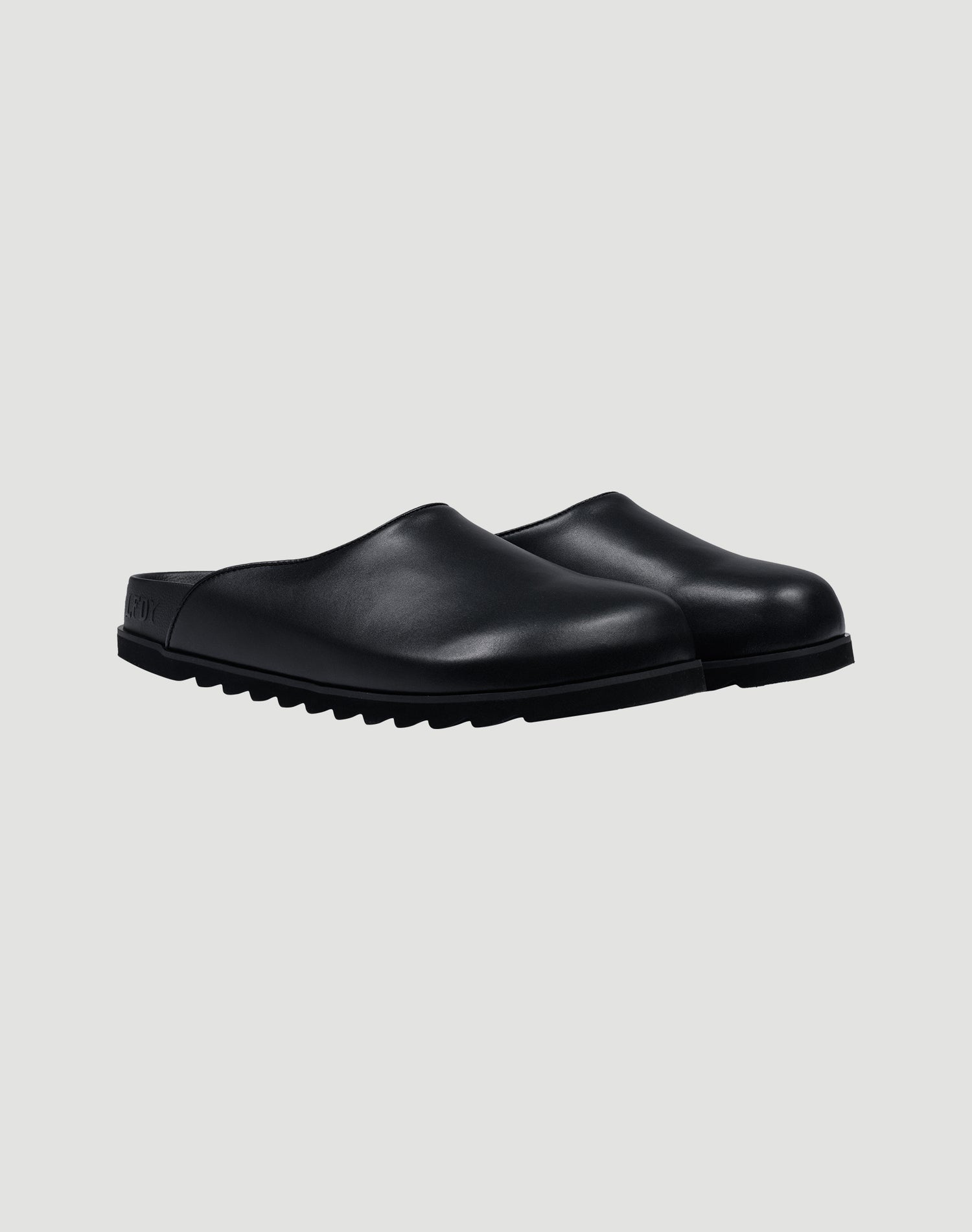 The LFDY Mules by LIVE FAST DIE YOUNG are black slip-on clogs with closed toes, textured PU Sohle, and schwarze Innenmaterial, shown on a plain light gray background.