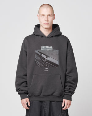 A person with a shaved head wears the LIVE FAST DIE YOUNG Benz Hooded, an oversize black hoodie with bold frontprint, paired with black pants against a plain light background.