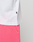 Close-up of a person wearing the LIVE FAST DIE YOUNG Basic Evidence Tee in white Oversize Fit (100% Baumwolle) with a black tag on the side seam and bright pink pants, hand in pocket, against a plain light background.