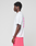 A person stands in profile against a plain background, wearing a LIVE FAST DIE YOUNG Basic Evidence Tee—an oversize fit white T-shirt with pink front and back print—and bright pink shorts.