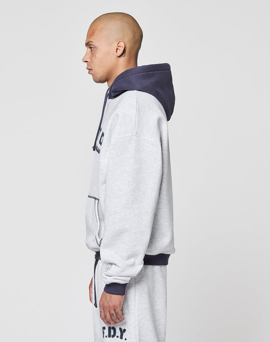 A person with a shaved head and face tattoos wears the oversized LIVE FAST DIE YOUNG LFDY District Hooded hoodie with contrasting hood and matching sweatpants, standing in profile against a plain white background.