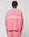 Seen from behind, a person with short braided hair wears the LIVE FAST DIE YOUNG "Live Fast Boucle Sweater," an oversized pink knit with "LIVE FAST" in white on the back, paired with matching pink pants against a plain light background.