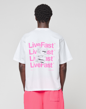 A person in an Oversize Fit, 100% cotton white Basic Evidence Tee by LIVE FAST DIE YOUNG, featuring repeated pink LiveFast™ prints front and back, is paired with bright pink shorts against a plain light background.
