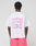 A person in an Oversize Fit, 100% cotton white Basic Evidence Tee by LIVE FAST DIE YOUNG, featuring repeated pink LiveFast™ prints front and back, is paired with bright pink shorts against a plain light background.