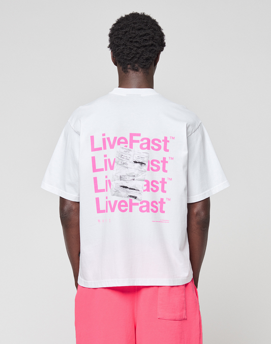 A person in an Oversize Fit, 100% cotton white Basic Evidence Tee by LIVE FAST DIE YOUNG, featuring repeated pink LiveFast™ prints front and back, is paired with bright pink shorts against a plain light background.