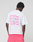 Wearing the Basic Evidence Tee by LIVE FAST DIE YOUNG—an oversized white T-shirt with a bold pink LiveFast backprint and crafted from 100% Baumwolle—the person pairs it with bright pink shorts, facing away against a plain backdrop.