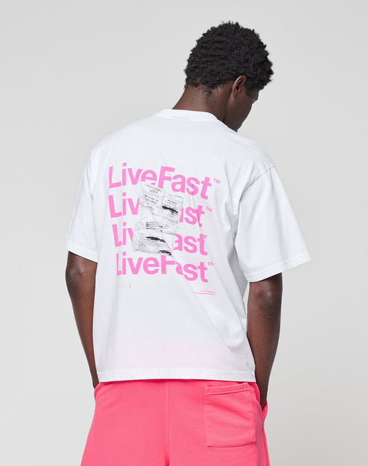Wearing the Basic Evidence Tee by LIVE FAST DIE YOUNG—an oversized white T-shirt with a bold pink LiveFast backprint and crafted from 100% Baumwolle—the person pairs it with bright pink shorts, facing away against a plain backdrop.