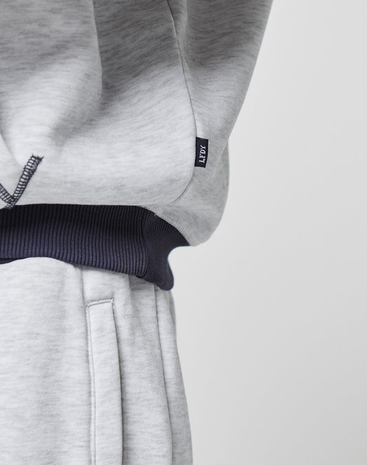 Close-up of a person in light gray LFDY District Hooded sweatpants and matching oversize hoodie by LIVE FAST DIE YOUNG, featuring a contrasting ribbed waistband and a small black tag with white lettering on the side seam.