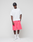 A man stands against a plain background wearing the LIVE FAST DIE YOUNG Basic Evidence Tee (100% Baumwolle, front and back print), a black cap, bright pink shorts, white crew socks, and white sneakers. He looks relaxed with his hands in his pockets.