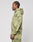A man with cornrows stands in profile wearing the LIVE FAST DIE YOUNG Camo Hooded Zip, featuring a green and beige splatter pattern, along with matching sweatpants, against a plain light background.