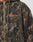 Close-up of a person wearing the LFDY Fleece Hooded Zip by LIVE FAST DIE YOUNG, a camouflage fleece jacket with drawstring hood, zipper, oversize fit, and an orange embroidered Live Fast logo on the left chest.