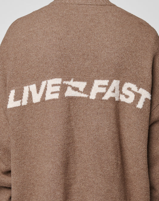 A close-up of the Live Fast Boucle Sweater by LIVE FAST DIE YOUNG shows its brown oversized fit, with "LIVE FAST" in large white block letters—A replaced by a lightning bolt—across the back for a bold effect.