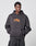 A person wearing the LIVE FAST DIE YOUNG Its Vulgar Center Hooded oversized dark hoodie, made from a soft cotton-polyester blend with orange ITS VULGAR text on the front, stands against a light gray background with hands in the front pocket.