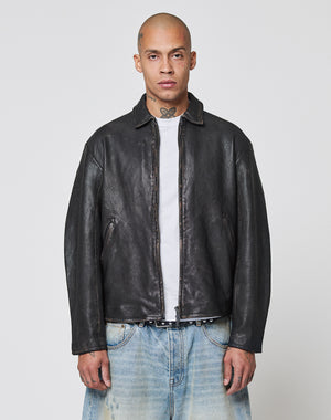 A person with a shaved head wears a black LIVE FAST DIE YOUNG LFDY Leather Jacket over a white shirt and light blue jeans, standing against a plain white background.