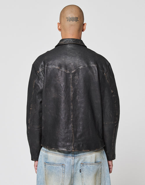 A person with a shaved head and a tattoo on the back faces away from the camera, wearing a black LFDY Leather Jacket by LIVE FAST DIE YOUNG and light blue denim jeans against a plain background.