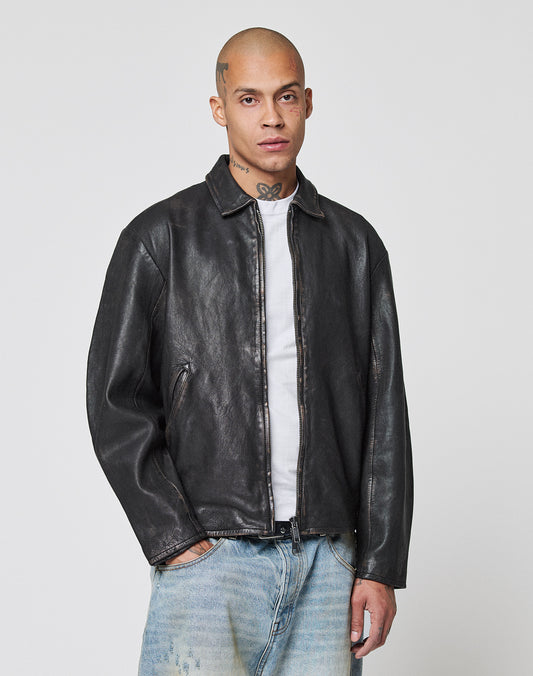 A person stands facing forward against a plain light background, wearing a black LIVE FAST DIE YOUNG LFDY Leather Jacket over a white t-shirt and faded blue jeans.