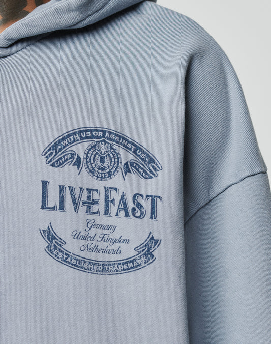 A close-up of the light blue LFDY 55 Hooded Zip by LIVE FAST DIE YOUNG in Oversize Fit, featuring a navy LIVE FAST graphic with Germany, United Kingdom, Netherlands, text banners, winged emblem, and stylish vintage wash.