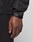 A close-up shows a persons hand and wrist wearing the LIVE FAST DIE YOUNG Live Fast Performance Rain Jacket with waterproof seams and an adjustable Velcro sleeve cuff, set against a plain, light-colored background.
