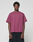 A person faces forward in a loose-fitting maroon Basic 210 Tee by LIVE FAST DIE YOUNG, featuring "LiveFast" on the chest, made from 100% cotton, paired with black shorts against a plain light gray background.