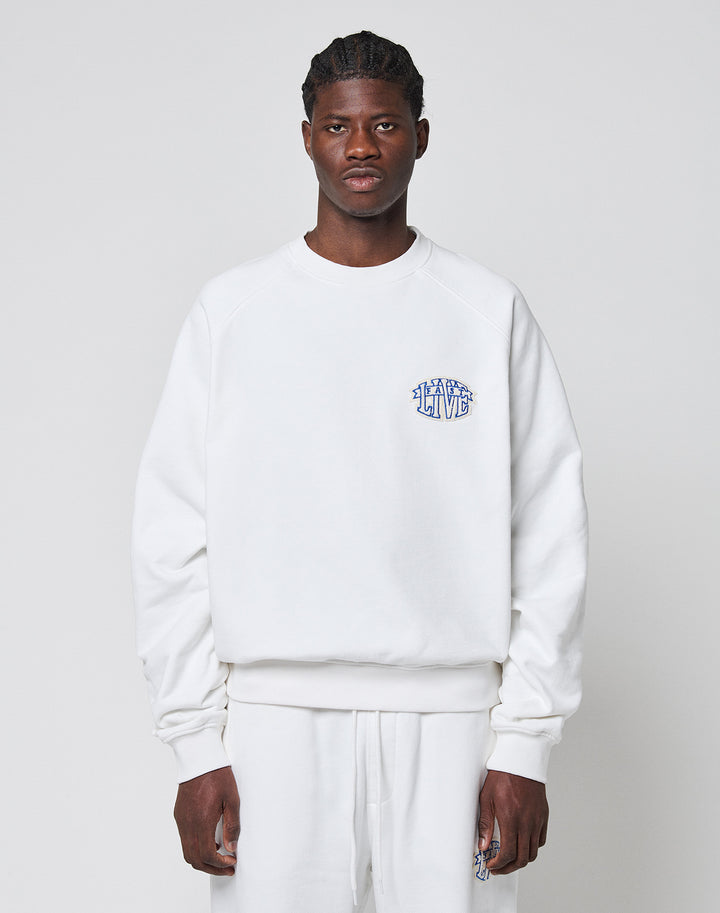 A person faces forward wearing a LIVE FAST DIE YOUNG LFDY Radiator Sweater in oversize white with matching pants. The Baumwolle Polyester sweater has a small blue LEARN TO LIVE graphic on the left chest. The background is plain light gray. | model