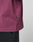 Close-up of a person wearing the LIVE FAST DIE YOUNG Basic 210 Tee in maroon, featuring an oversized fit and a small black tag on the side seam, paired with black pants. The background is plain and light-colored.