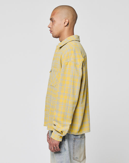 A person with a shaved head wears the LIVE FAST DIE YOUNG Vintage Flannel in yellow and gray plaid with light blue jeans, standing in profile against a plain white background.