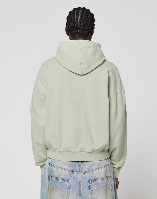 A person stands with their back to the camera, wearing a light green LIVE FAST DIE YOUNG LFDY District Hooded Zip and light blue denim jeans with visible back pockets. The background is plain and light-colored.