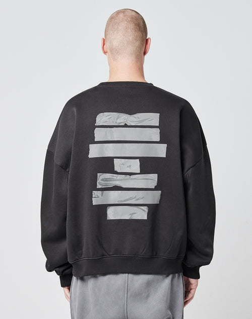 A person with a shaved head, seen from behind, wears the LIVE FAST DIE YOUNG Tape Sweater—an oversize black sweatshirt with five silver-grey stripes on the back. Its soft Baumwolle and Polyester blend stands out against a light background.