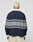 A person with short, bleached blonde hair is seen from behind in a LIVE FAST DIE YOUNG LFDY Striped Polo—an oversize fit navy sweater with two gray stripes, white collar and cuffs—paired with beige cotton-twill pants, against a plain light background.