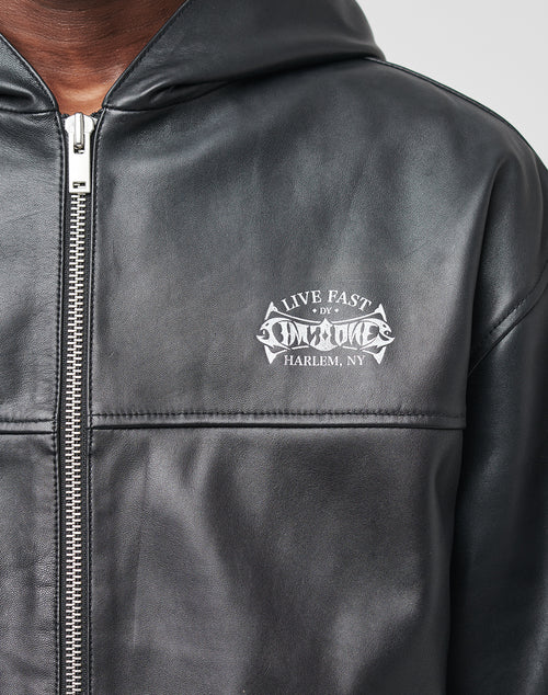 A close-up of a person wearing a black LIVE FAST DIE YOUNG Leather Hooded Jacket with a silver zipper and white chest logo. For lasting style, professional leather cleaning is recommended.