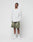 Against a plain white backdrop, a man wears the LIVE FAST DIE YOUNG Basic Longsleeve in light gray with an oversize fit, styled with olive green shorts, white crew socks, and white sneakers. His hands are in his pockets and he has a neutral expression.