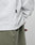 Close-up of a person in an oversize fit white LIVE FAST DIE YOUNG Basic Longsleeve (100% Baumwolle) with a small black IFPY tag and subtle logo-print, paired with olive green pants; the persons arm is bent behind their back.