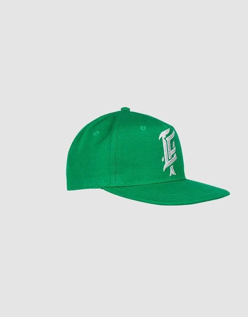 A green LF Rhinestone Cap by LIVE FAST DIE YOUNG aus Baumwolle with a flat brim, featuring a large white stylized letter L in Logo-Stick on the front, displayed against a plain light gray background.