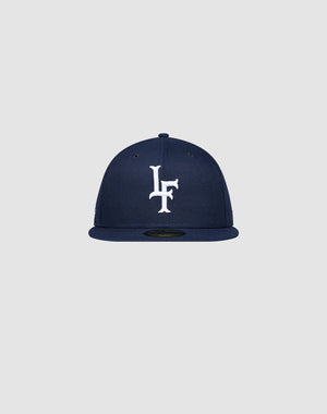 The LFDY x New Era 59Fifty Paris Fitted Cap by LIVE FAST DIE YOUNG features a navy blue design with white LF embroidery on the front and a flat brim, displayed on a plain light gray background. Größentabelle available for sizing.