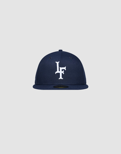 The LFDY x New Era 59Fifty Low Profile Paris cap by LIVE FAST DIE YOUNG features a navy blue design, flat brim, and white LF logo on the front, displayed against a plain light gray background.