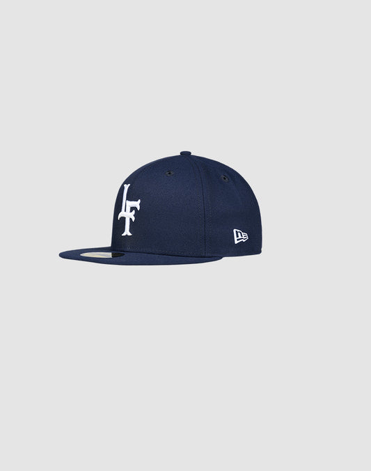 The LFDY x New Era 59Fifty Low Profile Paris cap by LIVE FAST DIE YOUNG features a navy blue design with a white LF logo on the front and New Era branding on the side, displayed against a plain light gray background.