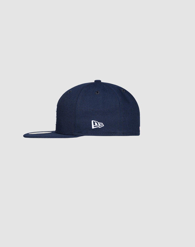 A side view of the LFDY x New Era 59Fifty Low Profile Paris fitted cap by LIVE FAST DIE YOUNG in navy blue, showing a small white embroidered logo on the left panel, set against a light gray background.