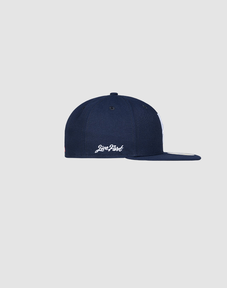 A navy blue LFDY x New Era 59Fifty Low Profile Paris fitted cap by LIVE FAST DIE YOUNG is shown from the side, with white "Live Fast" embroidery above the back opening, set against a plain light gray background.