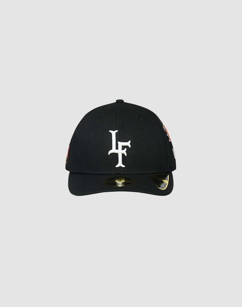 The LFDY X NEW ERA 59FIFTY LOW PROFILE by LIVE FAST DIE YOUNG is a black fitted cap with a white LF logo embroidered on the front, shown against a plain light gray background. A sticker appears on the low profile brim.