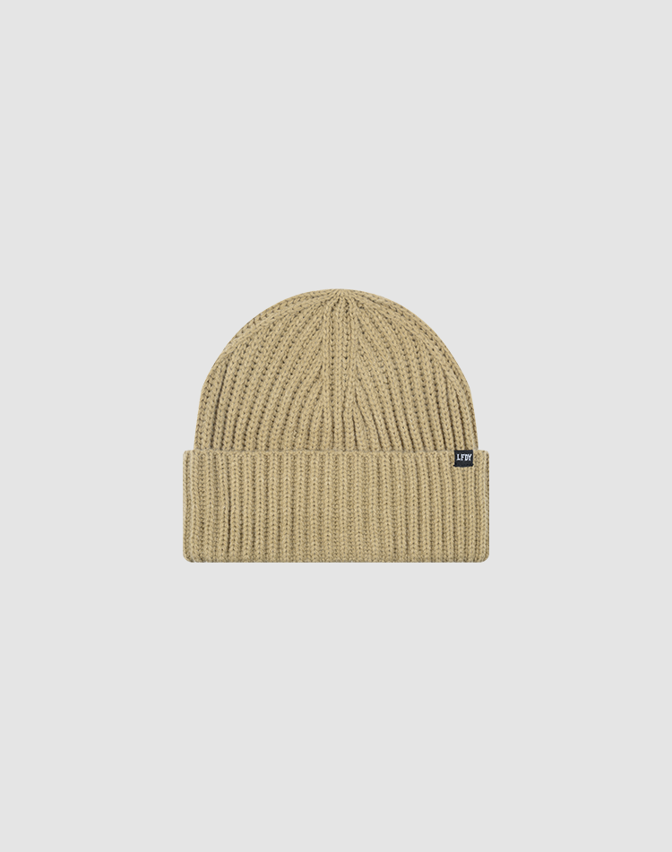The LIVE FAST DIE YOUNG Washed Rib Knit Beanie in beige features a folded brim, small black flag label on the side, and is crafted from soft polyamide. One Size. Displayed on a plain white background.