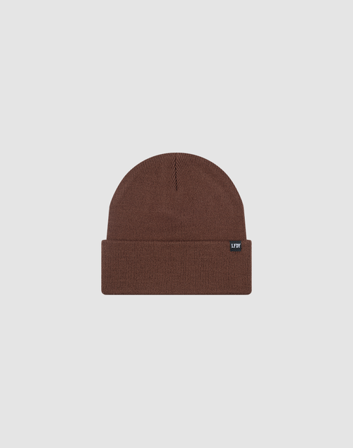 The LIVE FAST DIE YOUNG Basic Beanie is a brown knit, one-size hat with a folded cuff and a small rectangular black flag-label with white text on the cuff, shown on a plain light gray background.