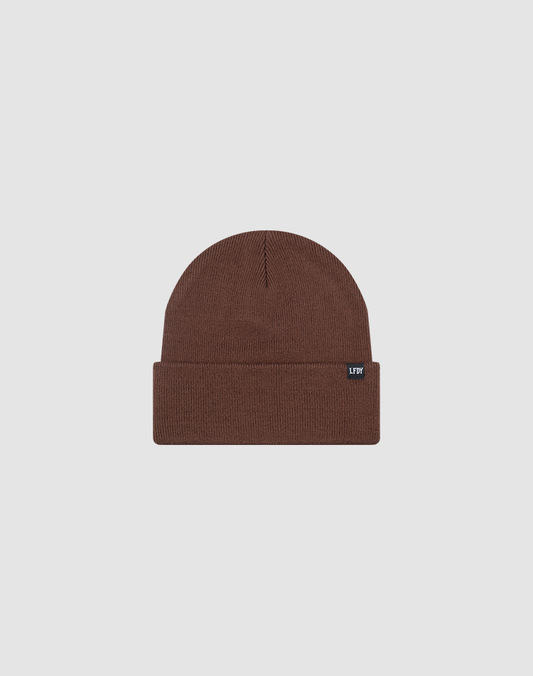 The LIVE FAST DIE YOUNG Basic Beanie is a brown knit, one-size hat with a folded cuff and a small rectangular black flag-label with white text on the cuff, shown on a plain light gray background.