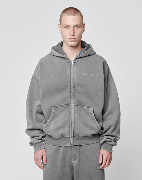 A person with short hair is wearing the LIVE FAST DIE YOUNG Basic Script Hooded Zip in gray with logo embroidery and matching sweatpants, standing against a plain light gray background.