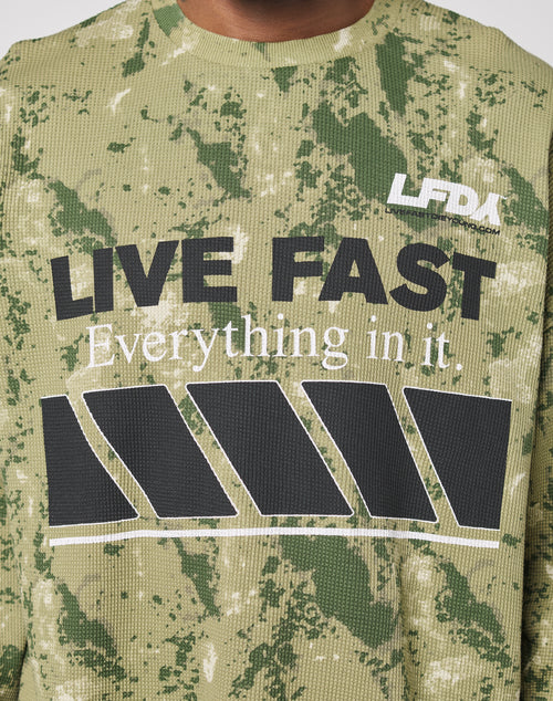 A close-up of the LFDY Racing Waffle Longsleeve by LIVE FAST DIE YOUNG—green camouflage, oversize fit, bold “LIVE FAST” and “Everything in it.” print, large black diagonal bars, and a white LFDA logo on the front.