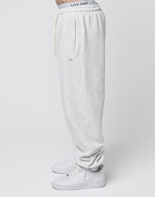A person wearing the Basic Loose Jogger in light gray by LIVE FAST DIE YOUNG, featuring a loose fit and LF DY logo, white sneakers, and a visible waistband that reads LIVE FAST, stands sideways against a plain background.