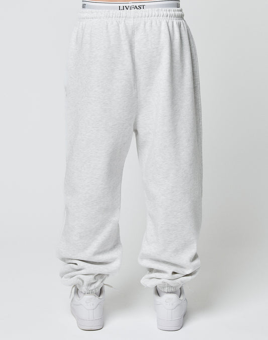 Model wears the LIVE FAST DIE YOUNG Basic Loose Jogger in light gray with Elastik-Bund and subtle logo, white LIVFAST waistband showing, paired with white sneakers, photographed from behind against a plain background.