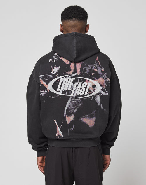 A person faces away from the camera in an oversize black LFDY Canine Hooded Zip by LIVE FAST DIE YOUNG, made from Baumwolle Polyester. It features snarling dog graphics and bold silver LIVE FAST text on the back, hood up.
