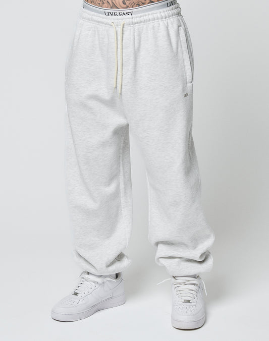 Someone models the LIVE FAST DIE YOUNG Basic Loose Jogger in light gray with a Loose Fit and elastic waistband featuring LIVE FAST text, paired with white sneakers, standing against a plain white background.