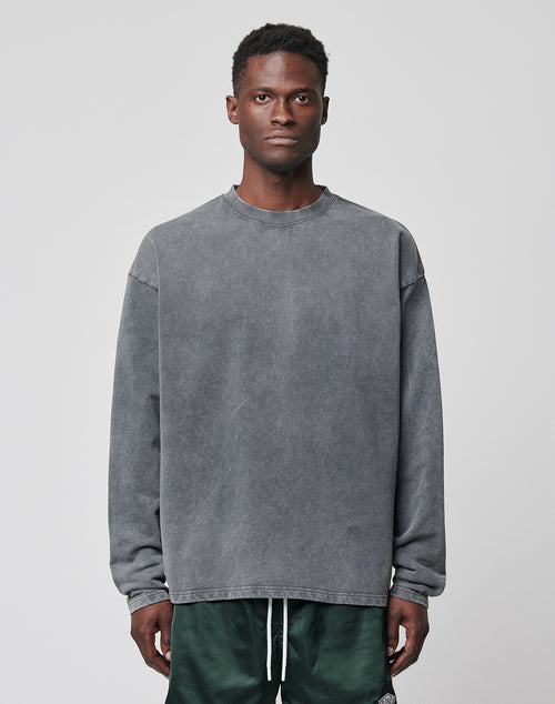 A man faces forward wearing a loose-fitting, vintage-washed gray LIVE FAST DIE YOUNG Basic Heavy Longsleeve sweatshirt and green shorts against a plain light gray background.