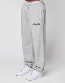 A model wears LIVE FAST DIE YOUNG Wide Cuff Jogger in light gray with "Live Fast" text on the left thigh and a comfy elastic waistband, styled with white sneakers. The photo shows the joggers waist to ankles against a plain white background.